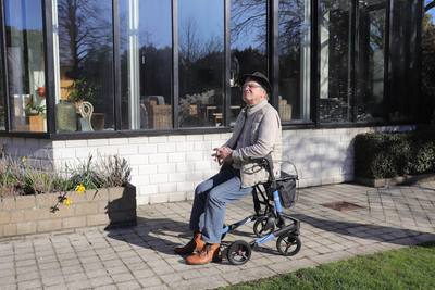Elderly man sitting on a walker outside a sunny day