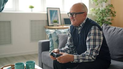 Joyful senior man playing video game alone entertaining at home enjoying gaming