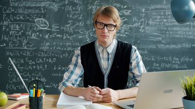 Portrait of serious handsome young man in glasses looking ay camera sitting