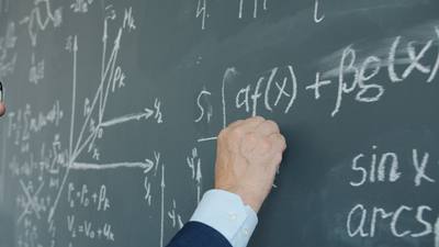 Close-up of male hand with chalk underlining formula on chalkboard in class,