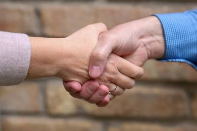 Two hands are engaged in a handshake. One hand has a ring on the finger, and