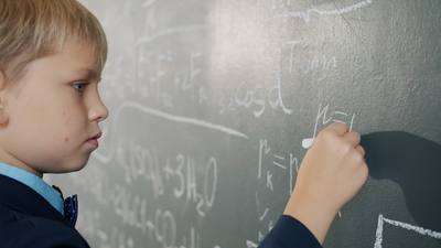smart schoolboy writing formulas on chalkboard studying alone indoors busy