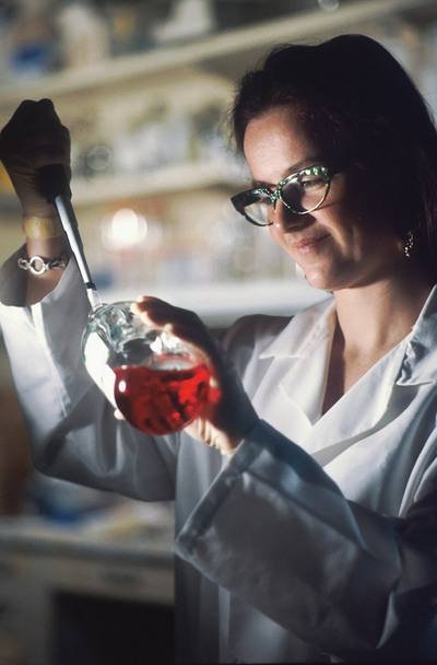 A female Caucasian scientist pipetting culture media in a flask.