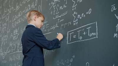 Low angle view of clever schoolboy writing formulas with chalk on blackboard