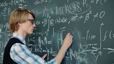 Smart man in glasses is writing equations on blackboard in class focused on
